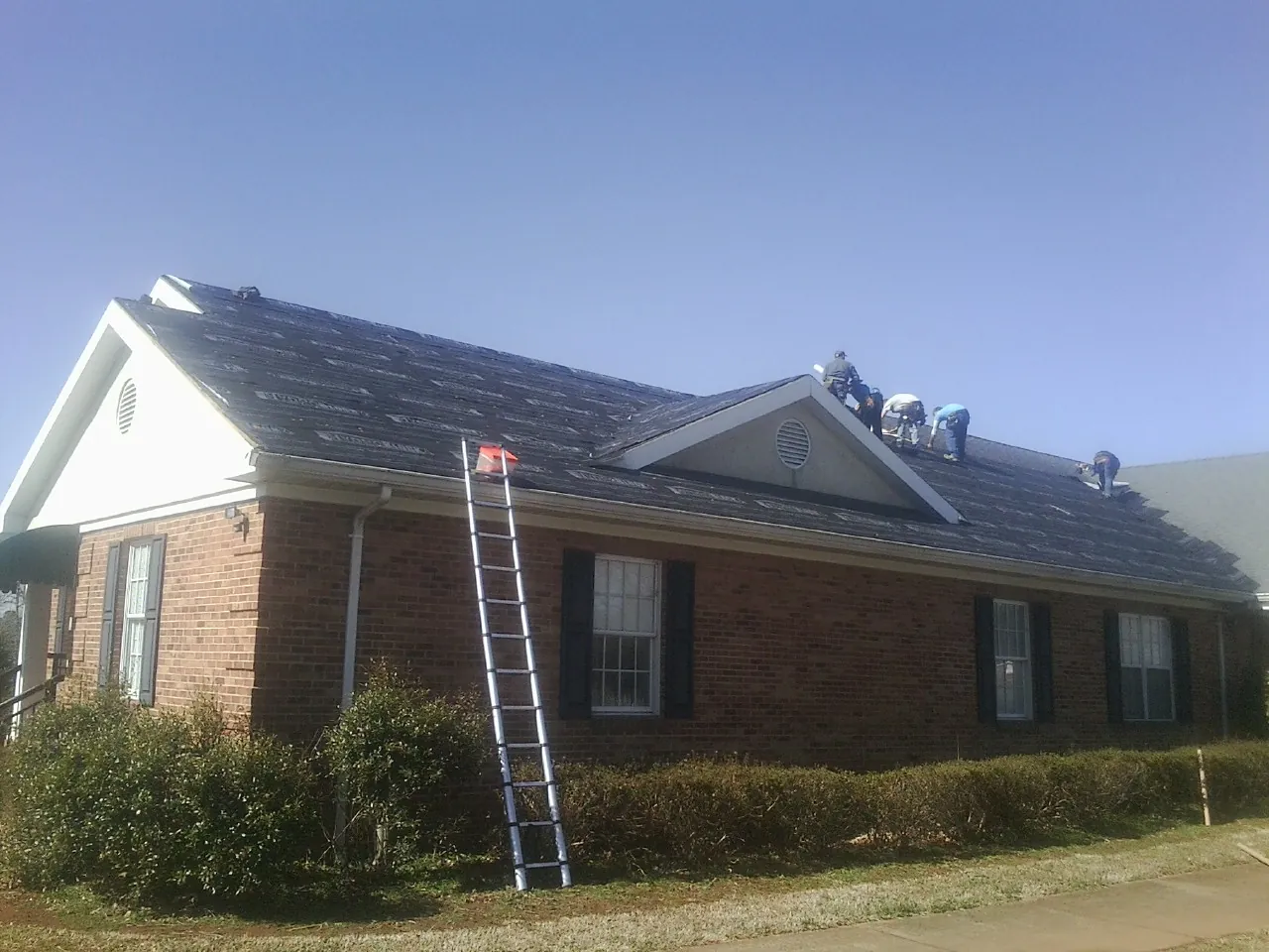 Crew tearing shingles off a brick ranch roof with a ladder set — Metal Roof Repair work by our crew in Byram