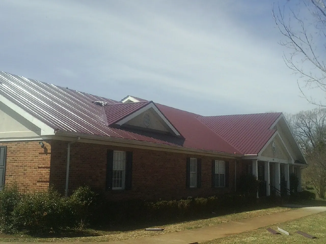 Red metal roof with gabled entries on a long brick building, from a Hail Damage Roof Repair job in Byram