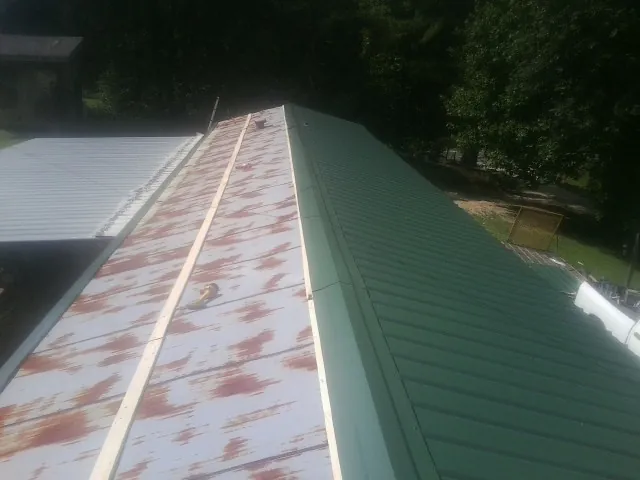 Old rusted panels beside newly installed green metal roofing — Wind Damage Roof Repair by Roofing Brothers in Byram