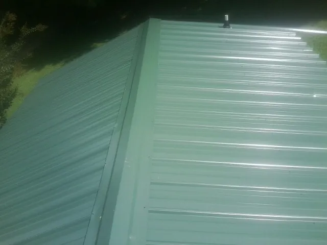 New green metal panels meeting at the ridge of a roof — Flat Roof Repair work by our crew in Byram
