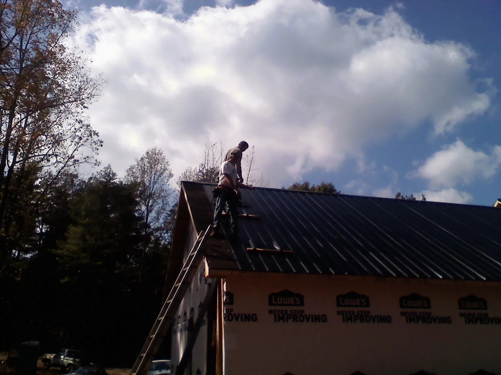 Roofer fastening dark metal panels high against a cloudy sky, from a Roof Inspection job in Byram