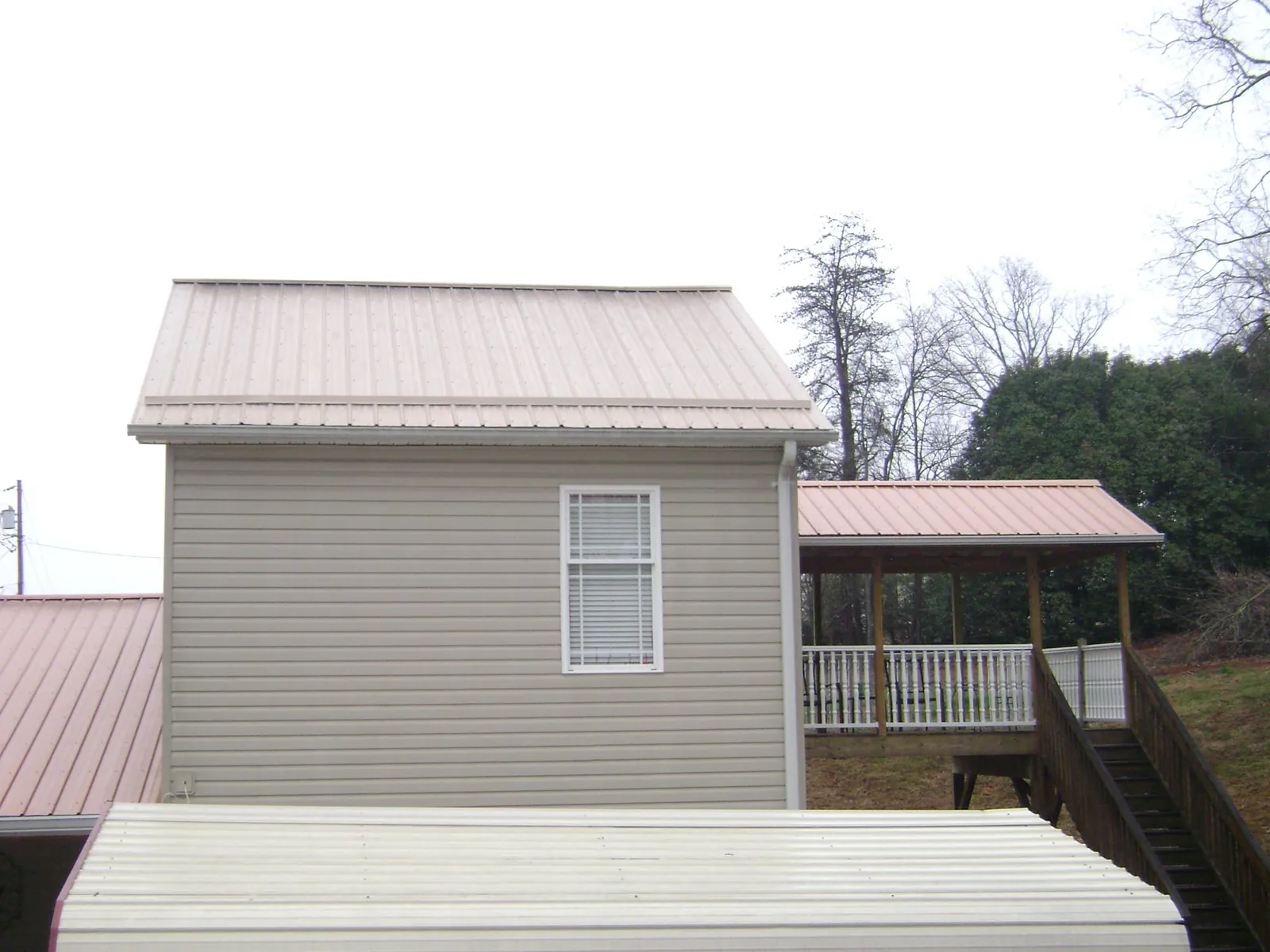 Tan metal roofs on a two story addition and attached porch, from a Roof Replacement job in Byram